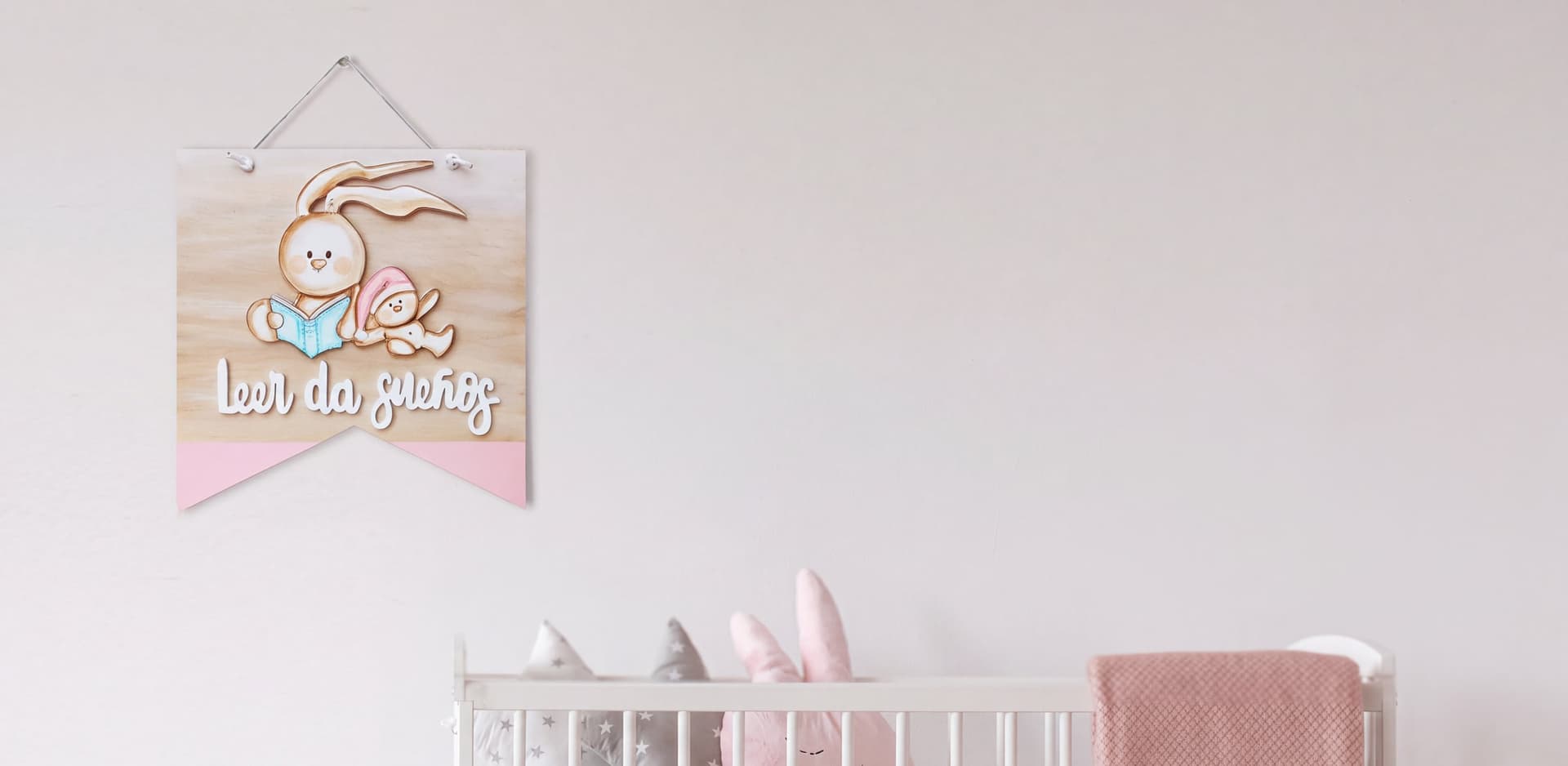 Banderola de madera «Leer da sueños» con dos conejitos colgada sobre una cuna